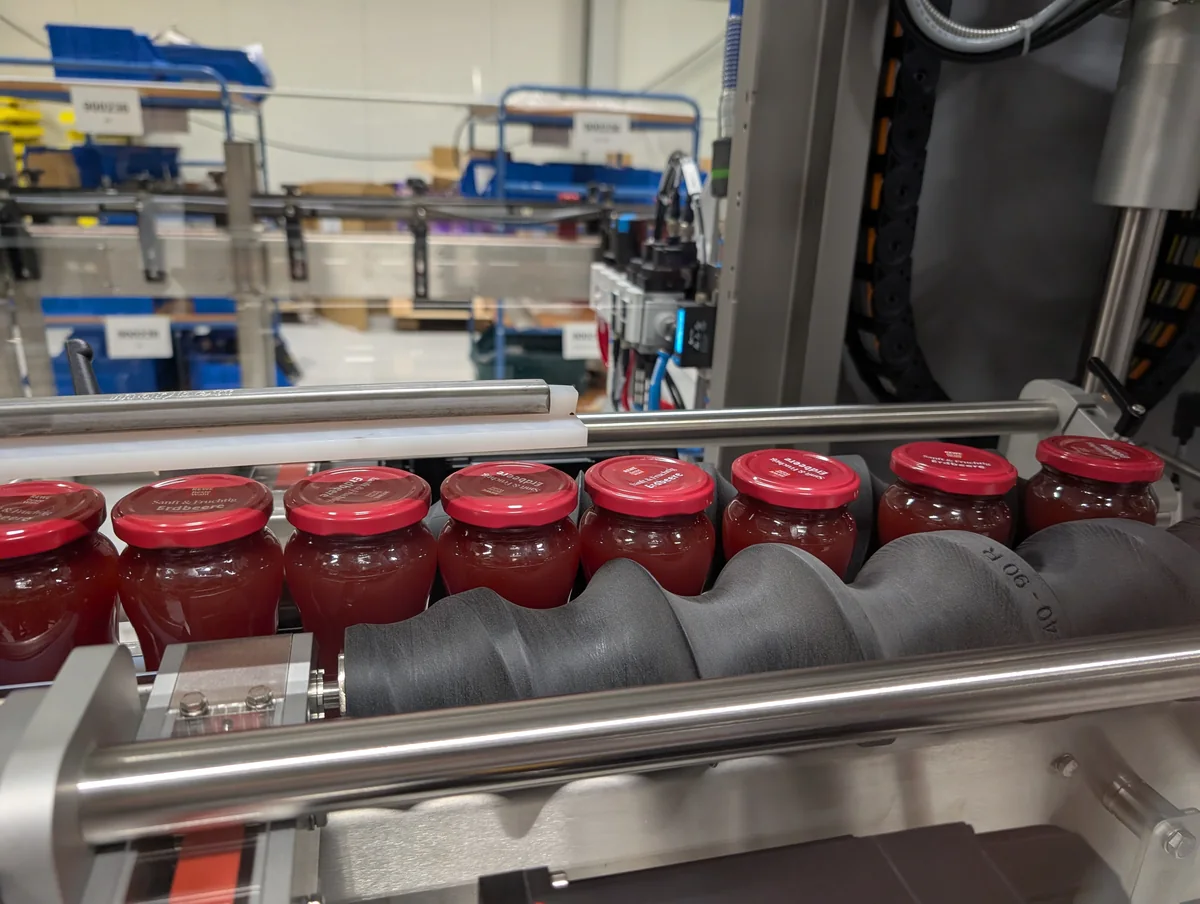 Black AddPack timing screw installed alongside red-lidded jars and stainless-steel machine guides